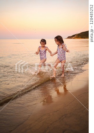 Sisters laughing and playing together on a serene beach at sunset Sisters laughing and playing together on a serene beach at sunset 128485252