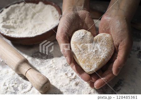 Baking concept. Caucasian female hands holding heart shaped dough. Baking concept. Caucasian female hands holding heart shaped dough. 128485361