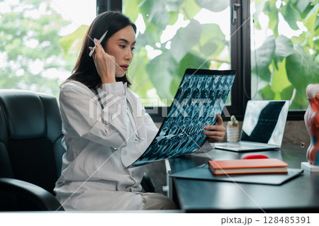 Female doctor examines X-ray in a bright office, surrounded by greenery, showcasing a blend of technology and nature. Female doctor examines X-ray in a bright office, surrounded by greenery, showcasing a blend of technology and nature. 128485391