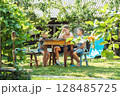 Three brothers are having lunch at a round wooden table in a lush garden, surrounded by greenery and sunlight 128485725