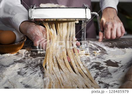 Caucasian female hands making fettuccine noodles using mechanical pasta machine Caucasian female hands making fettuccine noodles using mechanical pasta machine 128485979