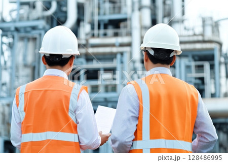 Engineers in Safety Gear Conducting Comprehensive Assessments of Industrial Facilities. Civil employees team review project plan at industrial facility factory building. Construction Industry. Outdoor 128486995