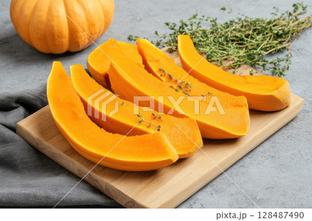 Cutting Fresh Pumpkins on Board. Baked pumpkin. Sliced raw Cucurbita maxima and spices for preparing soup, warm salad, fall dish. Thanksgiving food. Roasted vegetable in olive oil salt pepper, herbs. 128487490