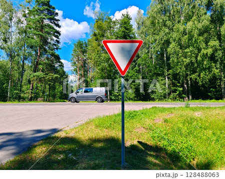 Road sign "give way" on the background of green. Road sign, secondary road on a country highway 128488063