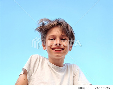 Closeup portrait of smiling school boy looking at camera. portrait of a happy Caucasian teenager boy against a blue sky 128488065