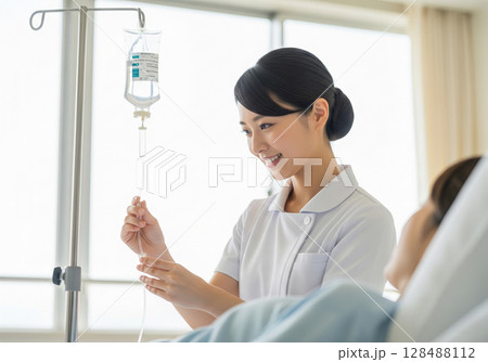 患者に点滴を行なう白衣の日本人女性看護師 患者に点滴を行なう白衣の日本人女性看護師 128488112