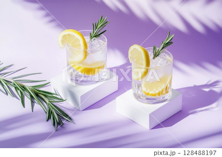 Refreshing lemon drink on purple. Summer refreshing lemonade drink or alcoholic cocktail with ice, rosemary, lemon slices on the table. Fresh healthy cold lemon beverage. Water with lemon. Copy space 128488197