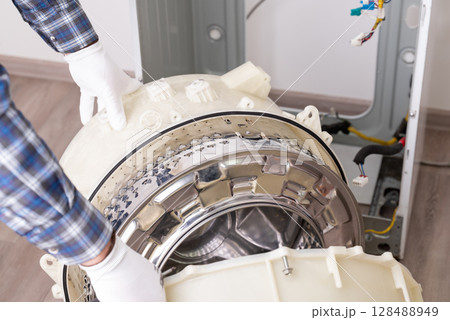 Repairing washer in service center. Handyman completely disassembled washing machine to change defective parts Repairing washer in service center. Handyman completely disassembled washing machine to change defective parts 128488949