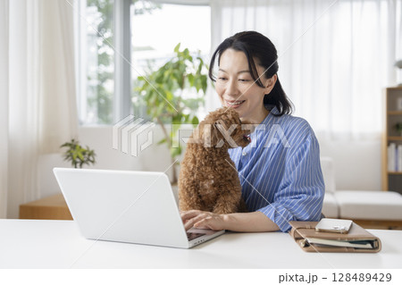 愛犬を抱いてパソコンで作業をするアラフィフの女性　在宅勤務イメージ 128489429