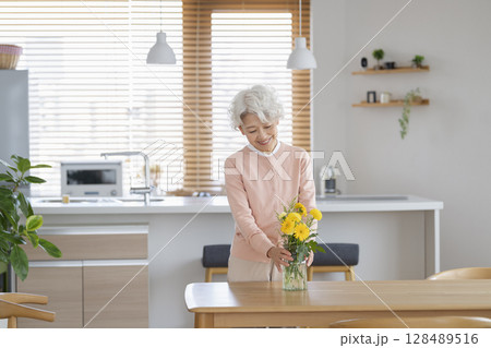 自宅のダイニングテーブルに花を飾るシニア女性 自宅のダイニングテーブルに花を飾るシニア女性 128489516