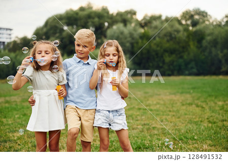 Boy with two girls, playing with bubbles. Kids are having fun on the field at daytime together 128491532