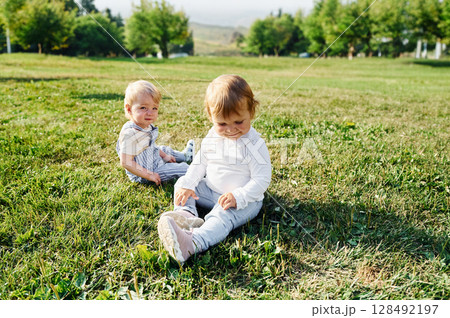 Two kids are sitting on the green field together 128492197