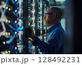 Technician examines complex data server systems in a dimly lit. 128492231