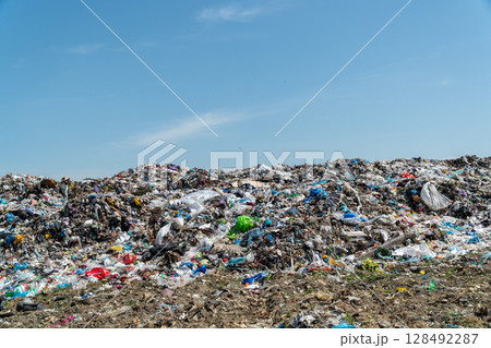 A large landfill filled with various types of waste under a clear blue sky shows the pressing need for effective waste management practices 128492287
