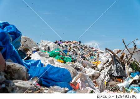 A large pile of assorted waste materials is seen at a landfill site under a clear blue sky, emphasizing the pressing issue of pollution 128492290