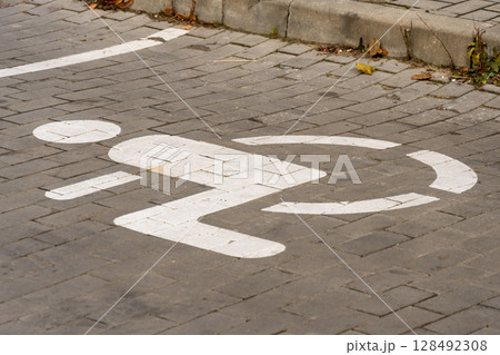 A parking space for individuals with disabilities features a clear symbol on the ground, located on a cobblestone street 128492308