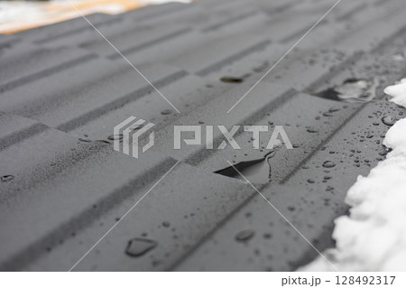 Melting snow creates small pools of water on the surface of newly installed metal roofing, showcasing the material and winter elements Melting snow creates small pools of water on the surface of newly installed metal roofing, showcasing the material and winter elements 128492317