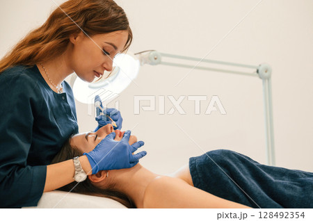Cosmetologist does injection for lips augmentation. Women's cosmetology in the beauty salon 128492354