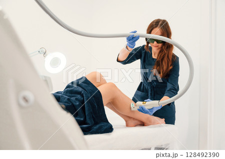 Procedure on the legs. Getting photo rejuvenation at cosmetology clinic. Women in beauty salon 128492390
