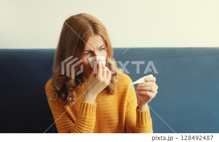Sick woman sneezing blow nose with tissue, measuring checking body temperature looks at thermometer Sick woman sneezing blow nose with tissue, measuring checking body temperature looks at thermometer 128492487