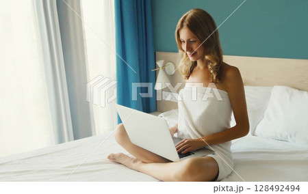 Happy young woman working on a laptop at home in the morning sitting on a bed in bedroom Happy young woman working on a laptop at home in the morning sitting on a bed in bedroom 128492494