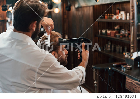 Using hair dryer. Man is visiting modern barber shop. Modern style Using hair dryer. Man is visiting modern barber shop. Modern style 128492631