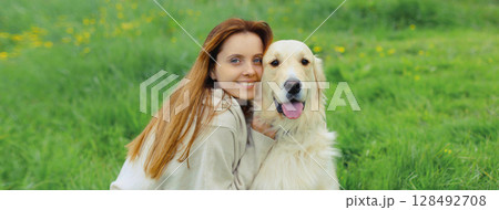 Happy owner young woman with Golden Retriever dog sitting on grass together in summer park Happy owner young woman with Golden Retriever dog sitting on grass together in summer park 128492708