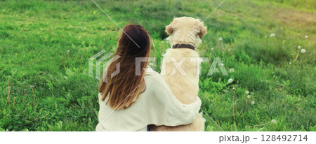 Happy owner young woman with Golden Retriever dog sitting on grass together in summer park 128492714