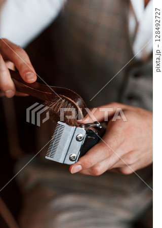 Cleaning hair clipper. Handsome barber is in the salon Cleaning hair clipper. Handsome barber is in the salon 128492727