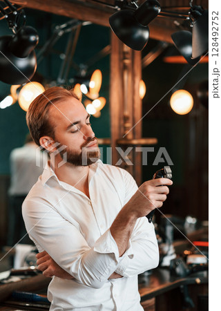 Hair clipper is in hand. Handsome barber is in the salon Hair clipper is in hand. Handsome barber is in the salon 128492752