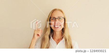 Portrait happy smiling mature woman pointing her fingers up on looking at camera, advertising text Portrait happy smiling mature woman pointing her fingers up on looking at camera, advertising text 128493021