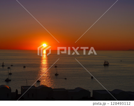 ギリシャ•サントリーニ島、イオから望むエーゲ海に沈む世界一の夕陽とそれを海上から眺める船の群れ ギリシャ•サントリーニ島、イオから望むエーゲ海に沈む世界一の夕陽とそれを海上から眺める船の群れ 128493112