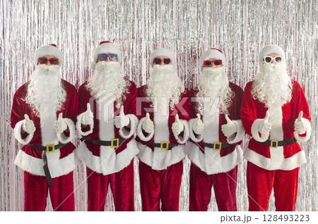 Happy funny people in Santa Claus costumes showing thumb up sign celebrating New Year and Christmas Happy funny people in Santa Claus costumes showing thumb up sign celebrating New Year and Christmas 128493223