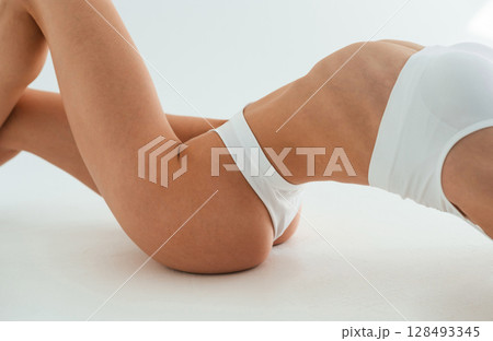 Close up view of belly, on the floor. Young woman with slim body type is in fitness clothes in the studio Close up view of belly, on the floor. Young woman with slim body type is in fitness clothes in the studio 128493345