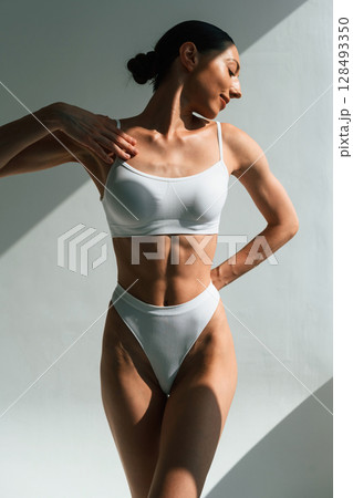 Shadow is on the body. Young woman in fitness clothes is in the studio Shadow is on the body. Young woman in fitness clothes is in the studio 128493350
