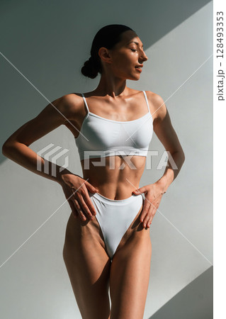 Showing abs. Young woman with slim body type is in fitness clothes in the studio 128493353