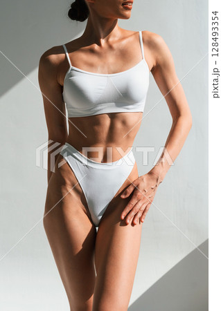 Showing abs. Young woman with slim body type is in fitness clothes in the studio 128493354