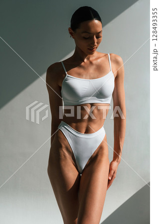 Showing abs. Young woman with slim body type is in fitness clothes in the studio 128493355