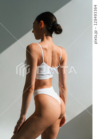 In the sunlight. Young woman with slim body type is in fitness clothes in the studio 128493364