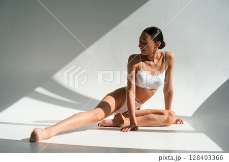 Daytime sunlight. Young woman with slim body type is in fitness clothes in the studio Daytime sunlight. Young woman with slim body type is in fitness clothes in the studio 128493366