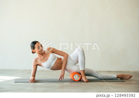 Using foam roller for exercises. Young woman with slim body type is in fitness clothes in the studio 128493392