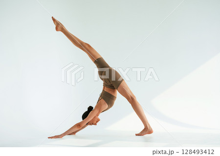 Working on the stretching of legs. Young woman with slim body type is in fitness clothes in the studio 128493412