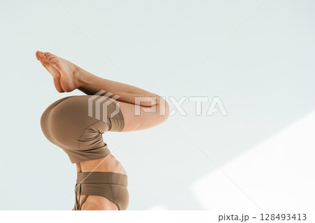 Doing head stand. Young woman with slim body type is in fitness clothes in the studio 128493413