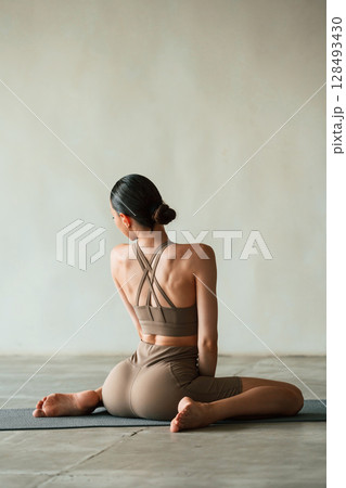 Flexible body, sitting, rear view. Young woman with slim body type is in fitness clothes in the studio 128493430