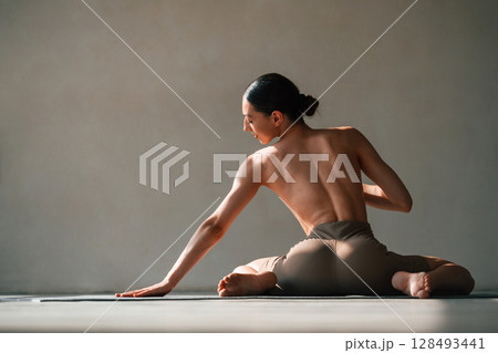 Without bra, sitting on the floor. Young woman with slim body type is in fitness clothes in the studio 128493441