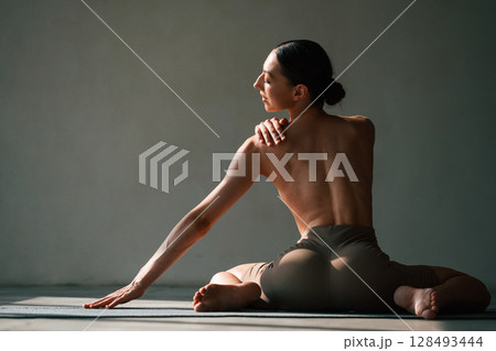 Without bra, sitting on the floor. Young woman with slim body type is in fitness clothes in the studio 128493444