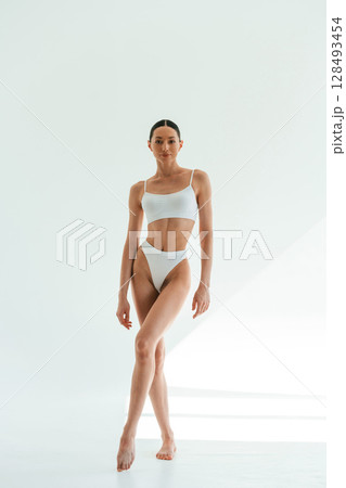 Standing and posing. Young woman with slim body type is in fitness clothes in the studio Standing and posing. Young woman with slim body type is in fitness clothes in the studio 128493454