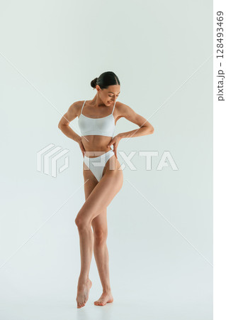 Against white background. Young woman with slim body type is in fitness clothes in the studio Against white background. Young woman with slim body type is in fitness clothes in the studio 128493469