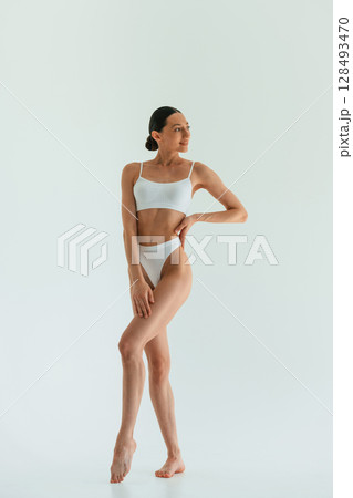 In white fitness clothes. Young woman with slim body type is in the studio 128493470