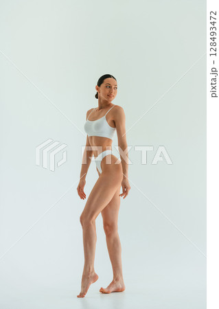 In white fitness clothes. Young woman with slim body type is in the studio 128493472